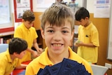 A student from Reservoir East Primary School holds up his class bank notes as part of a finance program.