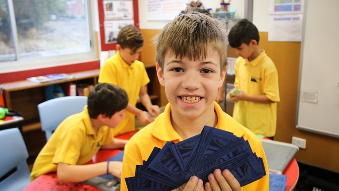 A student from Reservoir East Primary School holds up his class bank notes as part of a finance program.