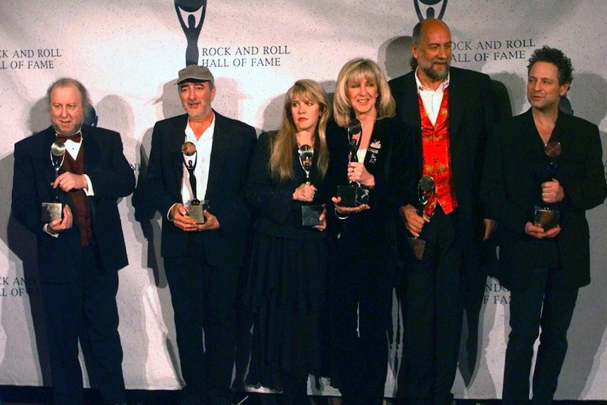 Three women and three men in formal wear line up and hold awards as they pose for a photograph