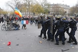 Paris protesters take photos and hide from police marching forward with riot gear on a dirty street.