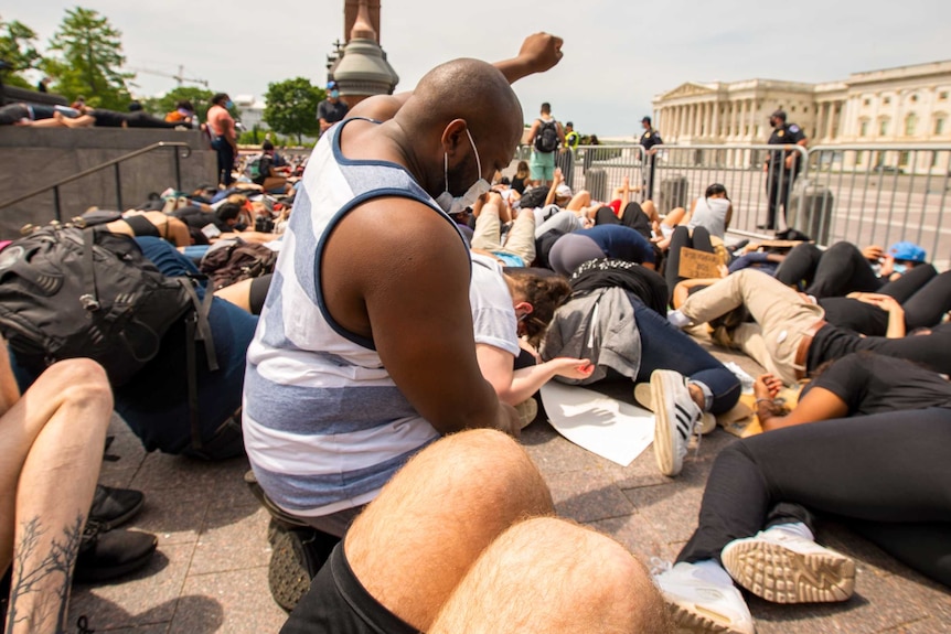 An African American protester kneels around people on the ground with his fist in the air