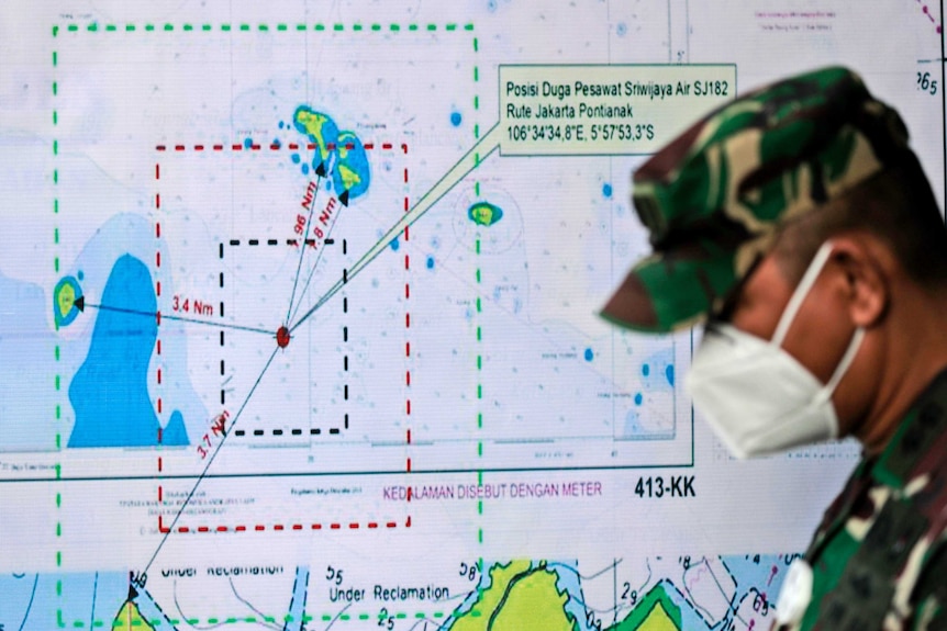 An Indonesian soldier walks past a map showing the location where the plane lost contact