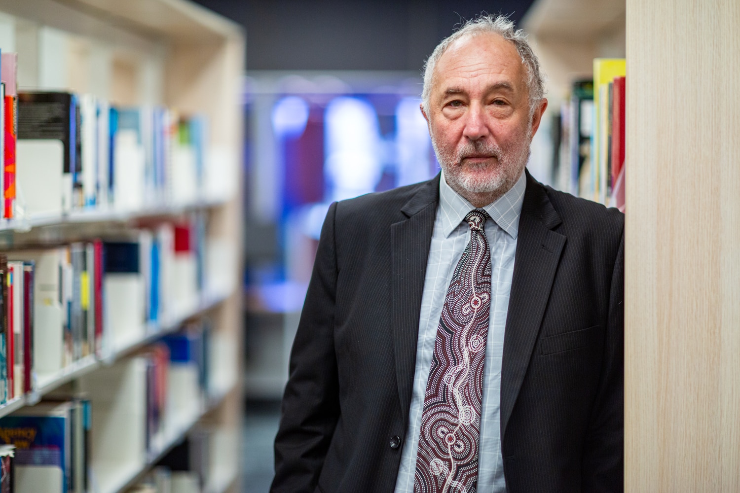 A middle-aged man in a dark suit stands in a library.