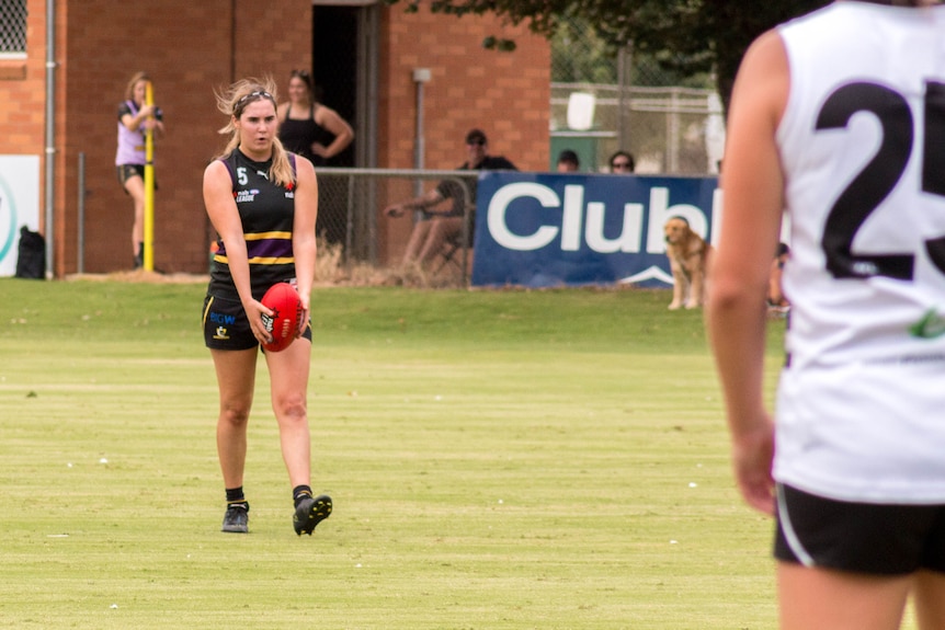 A young woman gets ready to kick an Australian rules football