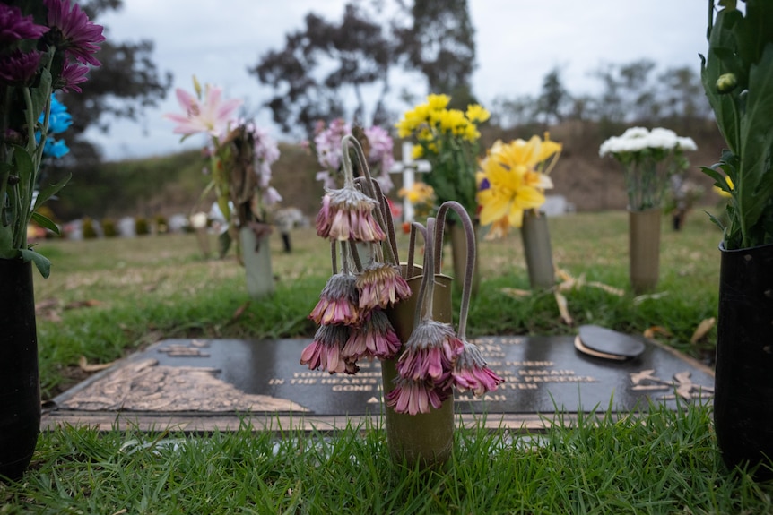 Flowers surround a grave. One bunch in the foreground is drooping.