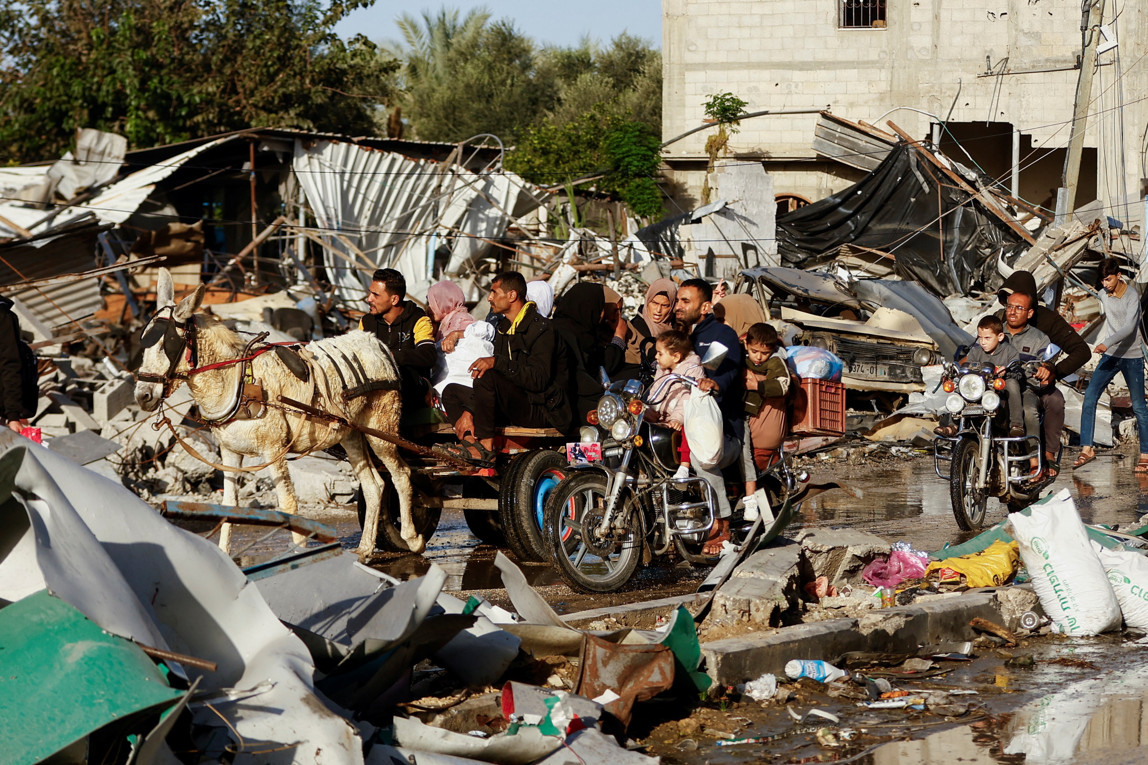 A family rides on cart pulled by a donkey through a street littered with debris