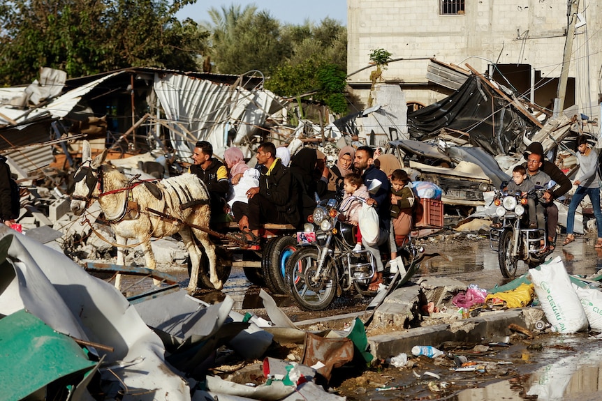 A family rides on cart pulled by a donkey through a street littered with debris