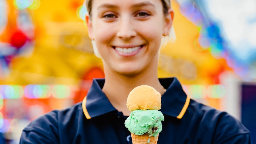 A woman holds a cone with two scoops of ice cream.