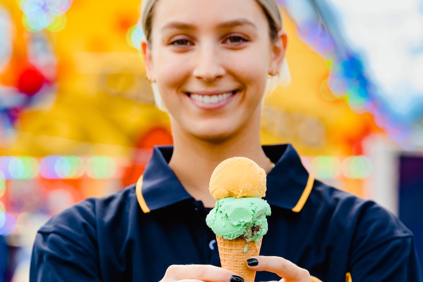 A woman holds a cone with two scoops of ice cream.