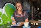 Woman in glasses at a cafe holding forms.