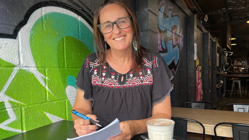 Woman in glasses at a cafe holding forms.