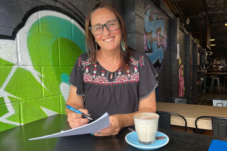 Woman in glasses at a cafe holding forms.