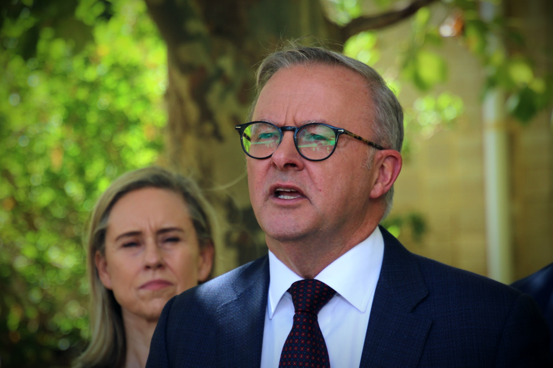 The Prime Minister stands in a leafy green area holding a press conference