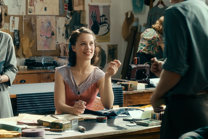 Colour still of Paula Beer smoking, seated at desk and smiling at man in 2018 film Never Look Away.