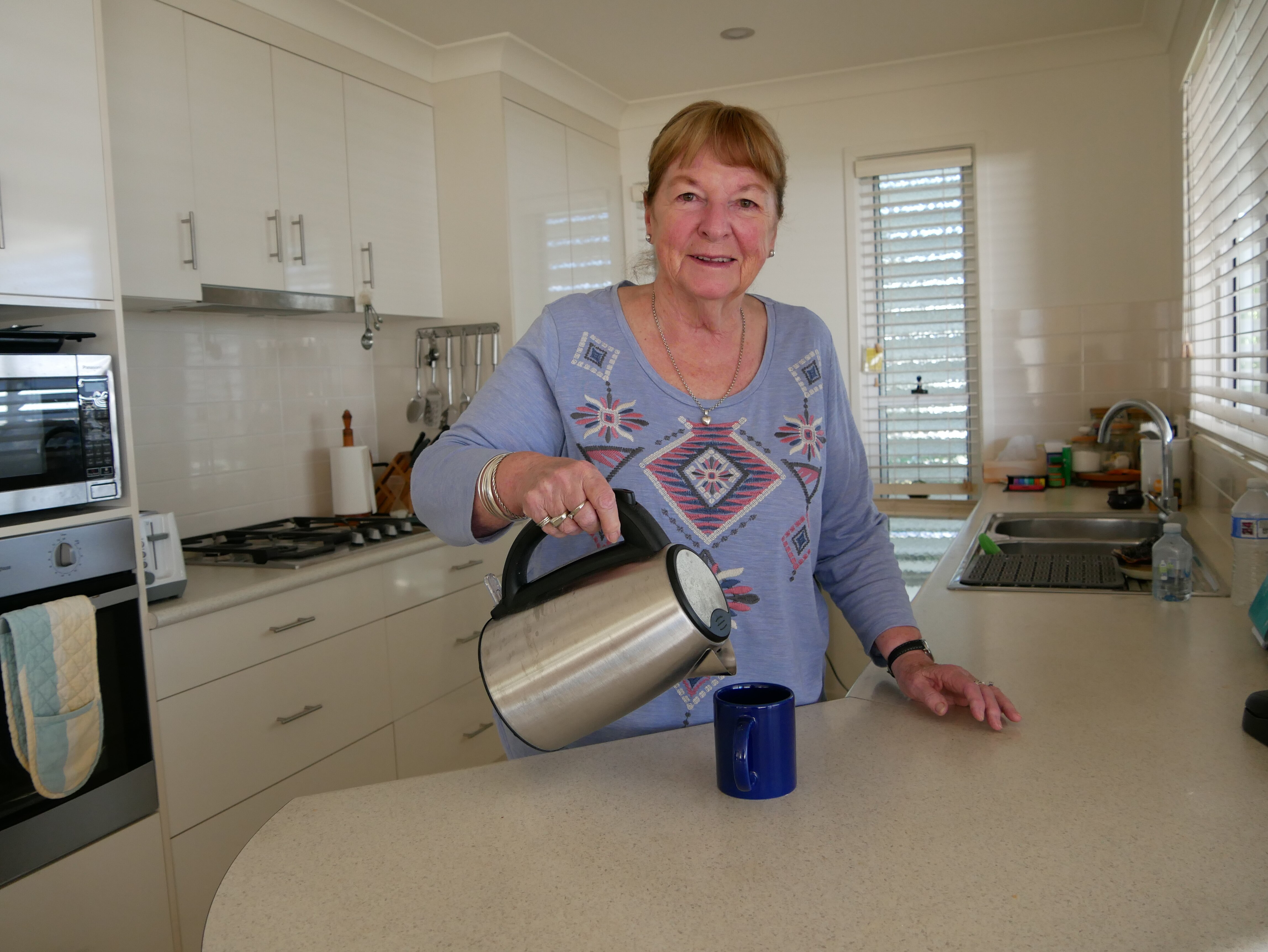 Older woman in the kitchen pouring a cup of tea