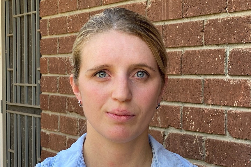 A woman wearing a blue top standing in front of a brick wall