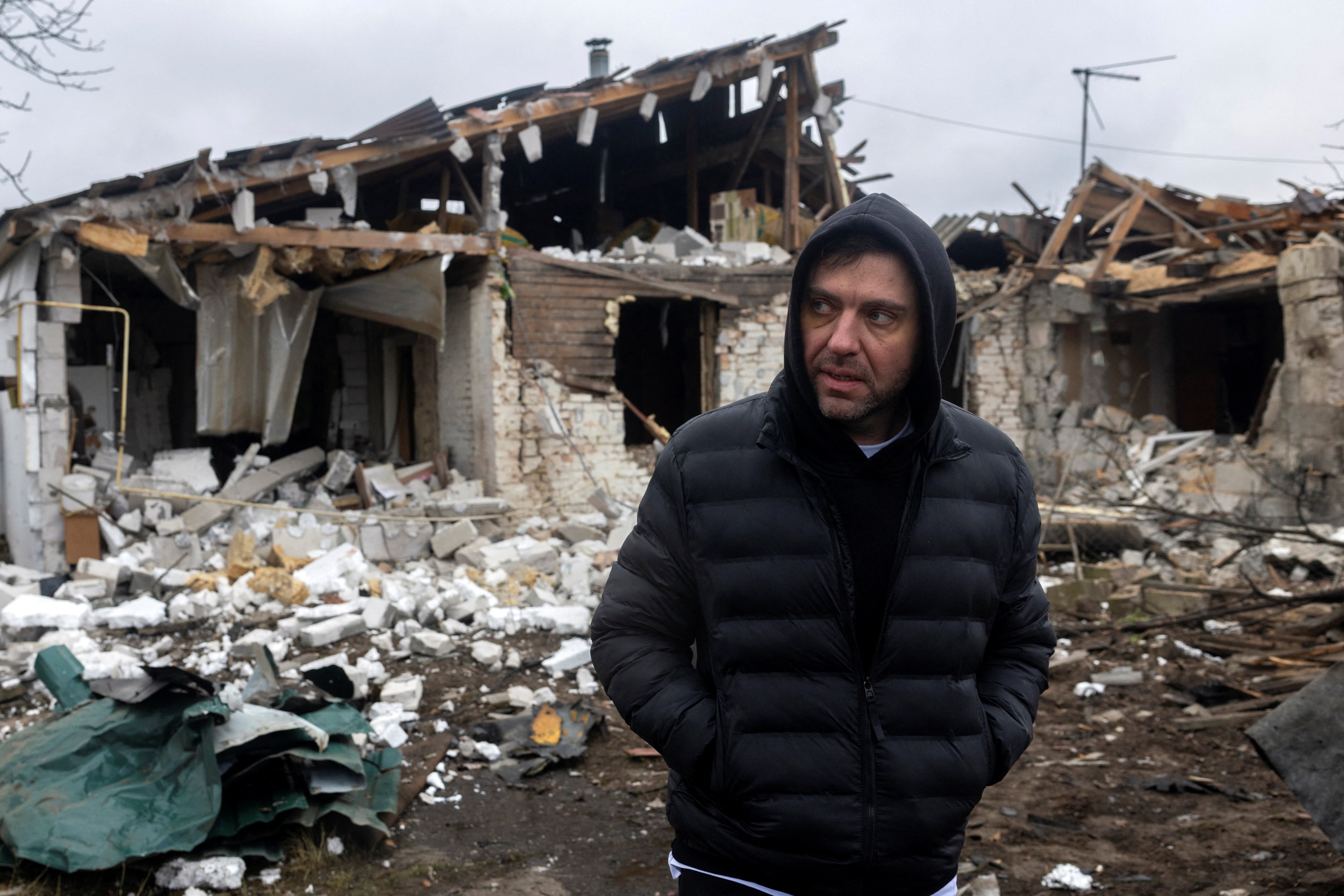 Um homem com capuz sai de uma casa gravemente danificada por um ataque de drone.