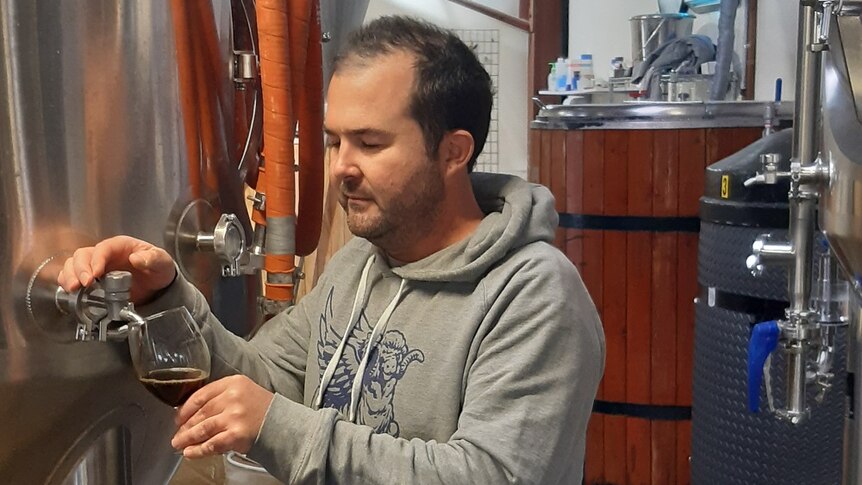 Man taps dark beer from stainless steel vat in brewery