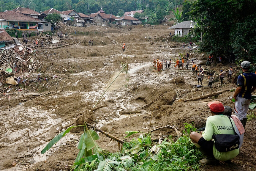 A landscape photo shows a hillside town decimated by a landslide as thick, brown, mud cakes a descending hilltop.