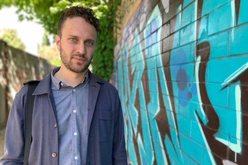 a man looks at the camera with a neutral expression.