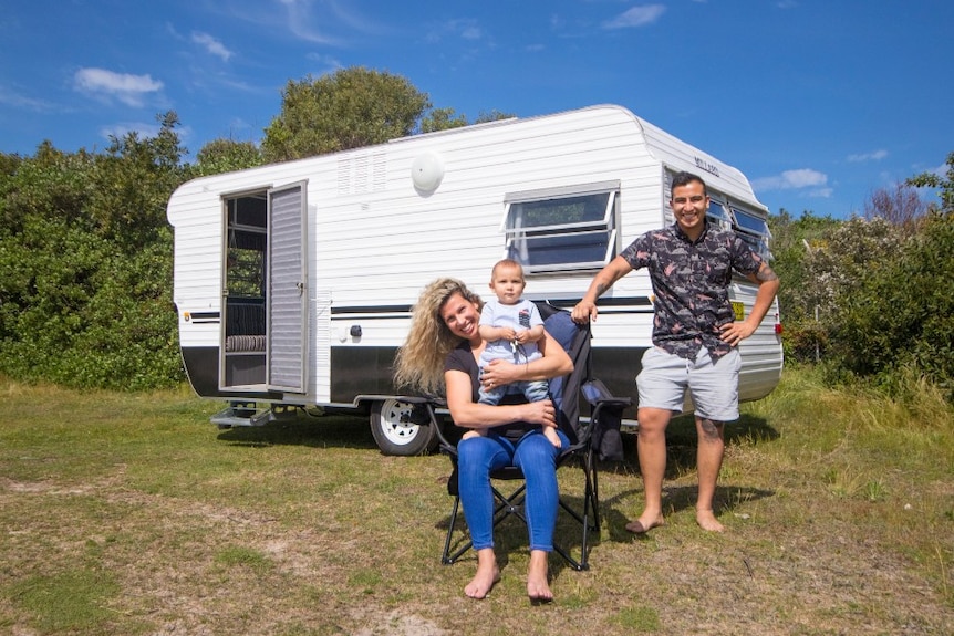 A young family stands in front of a Millard caravan at a beachside location.