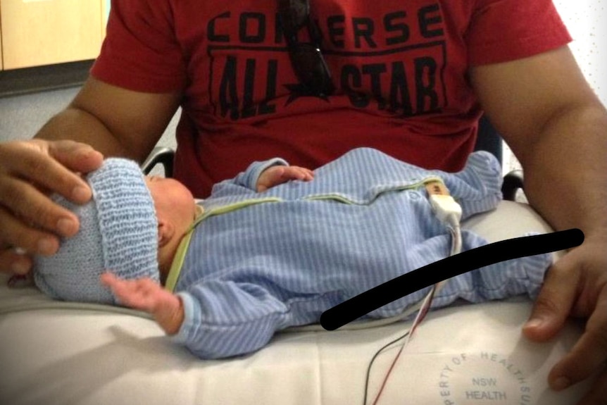 Father sitting beside his new born pre-term baby lying on a hospital bed in his little blue suit