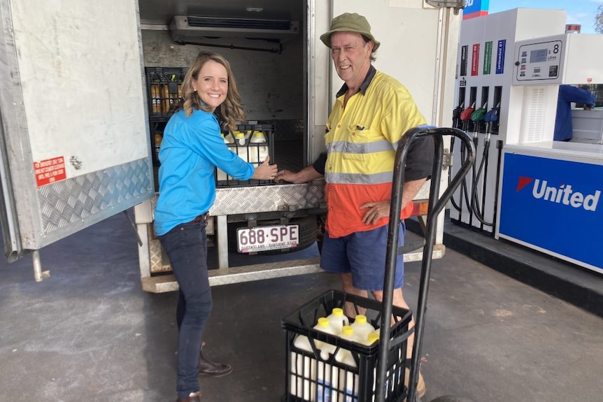 Male and female standing at the rear of a milk van. Female is mid-action pulling out a crate of milk from the boot. Both smiling