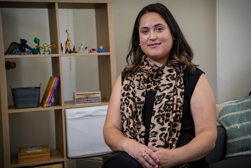 A woman wearing a black top sits in a consultation room, which has children's toys on a bookshelf in the background.