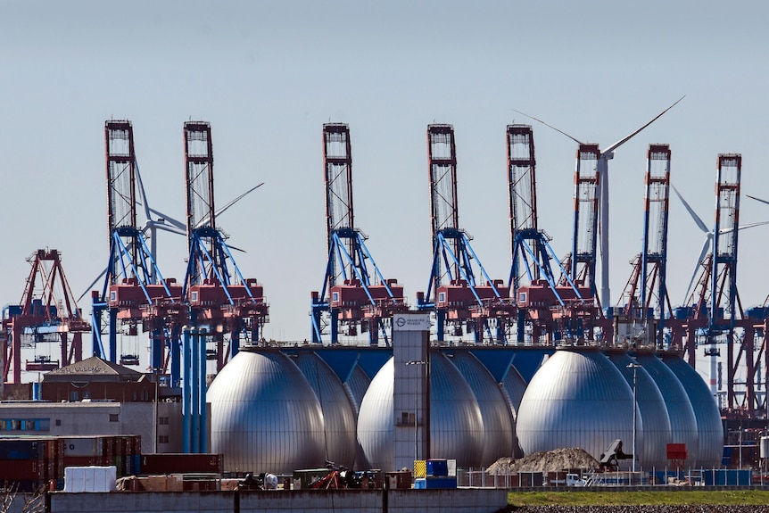 Три огромных серебряных резервуара для производства биогаза изображены в промышленном порту.