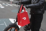 A doordash bag hangs from the handlebars of an electric scooter