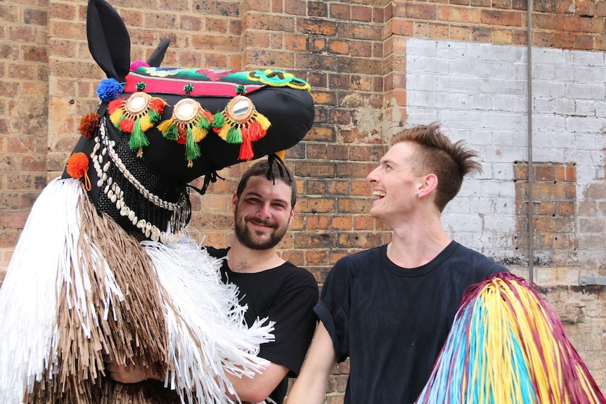 Two men holding the life-sized horse puppet they will wear in the dance.