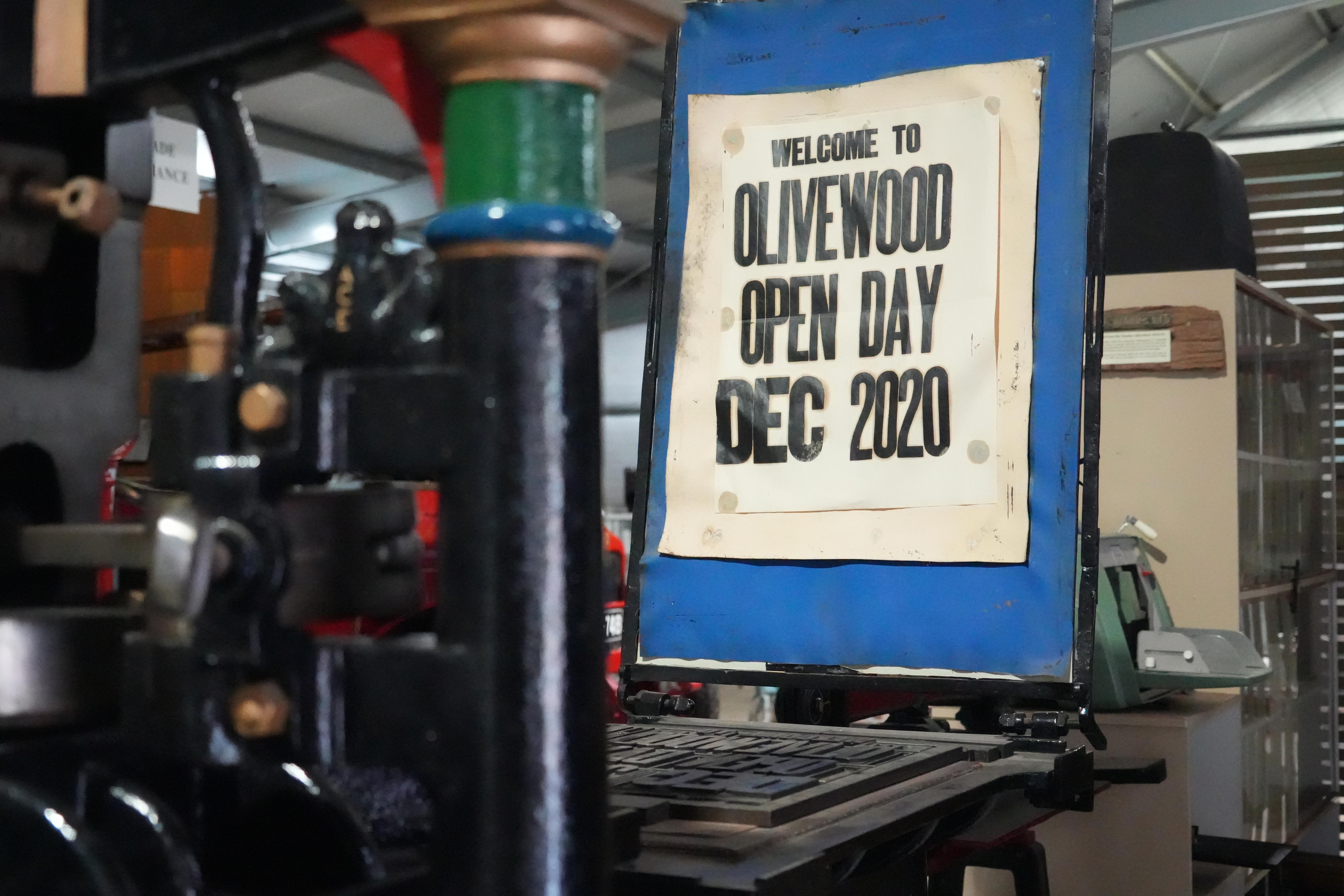 A paper sign saying "Welcome to Olivewood" sits at the back of an old printing press.