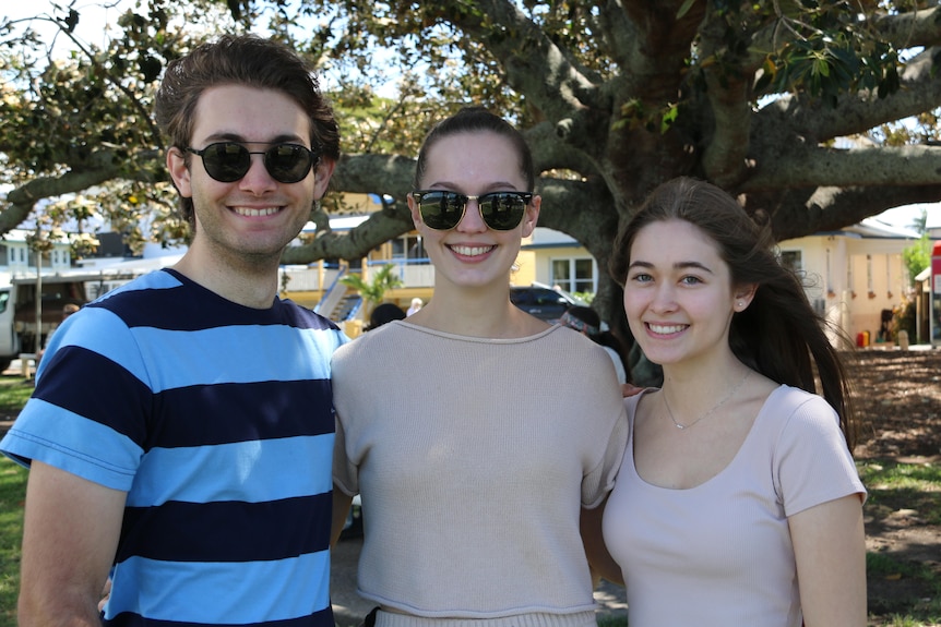 Three young people wearing sunglasses stand together under a tree
