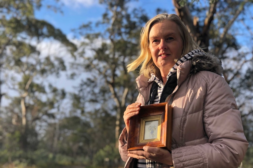 Robyn Lewis holding a frame of a painted orchid in Cambridge.