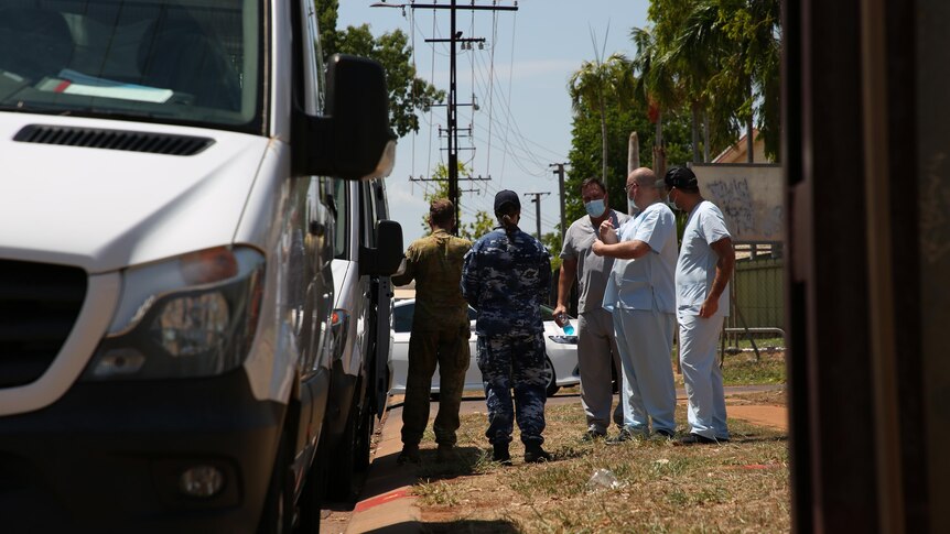 Two defence personnel speaking with health workers on a verge, next to a truck, in Katherine.