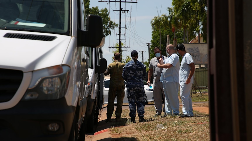 Two defence personnel speaking with health workers on a verge, next to a truck, in Katherine.