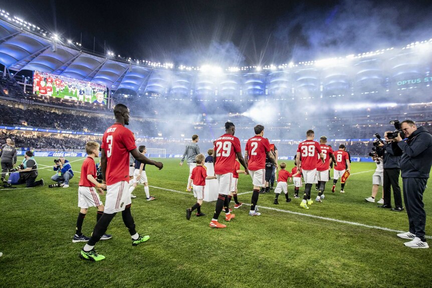 Manchester United and Leeds United walk out onto Perth Stadium under lights.