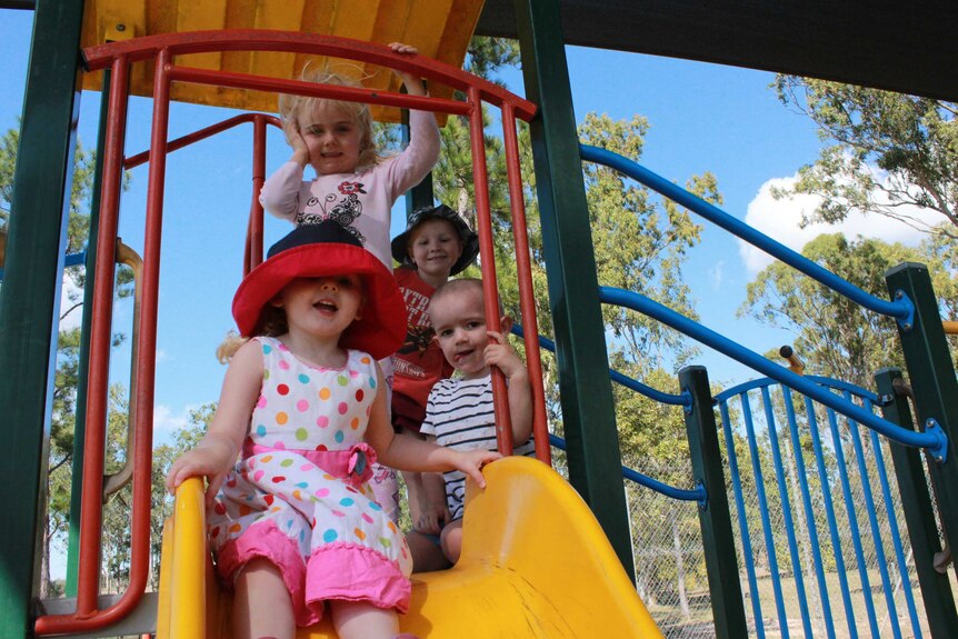 Four preschool aged children pose on a slippery slide.