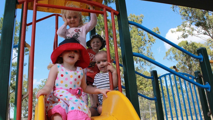 Four preschool aged children pose on a slippery slide.