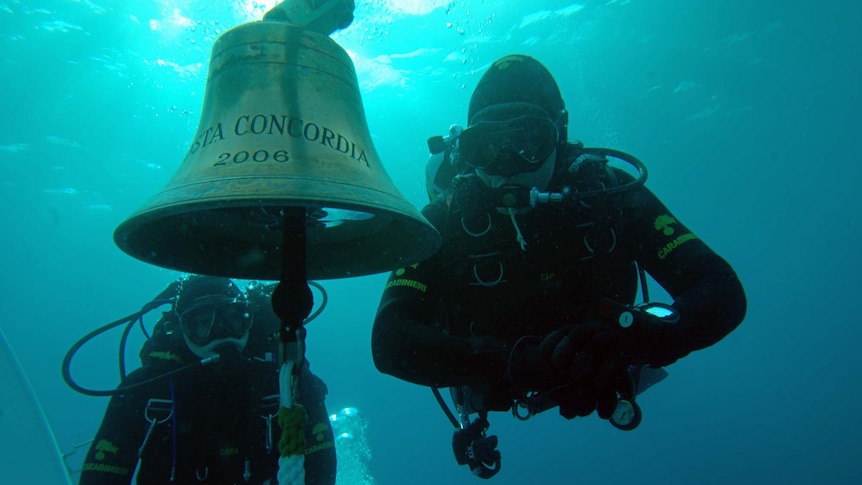 Italian Carabinieri divers pass by the bell of the stricken Costa Concordia luxury liner