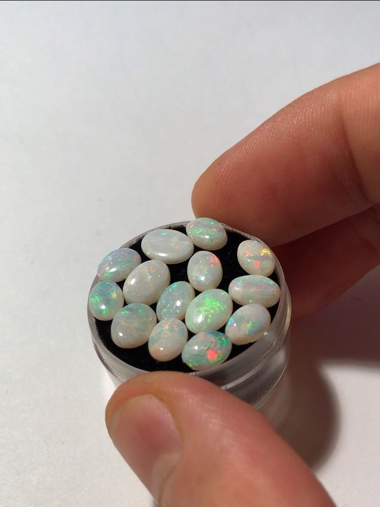 Small white-based opal with bright green, red, yellow and blue flashes sits in a small container ready for sale.