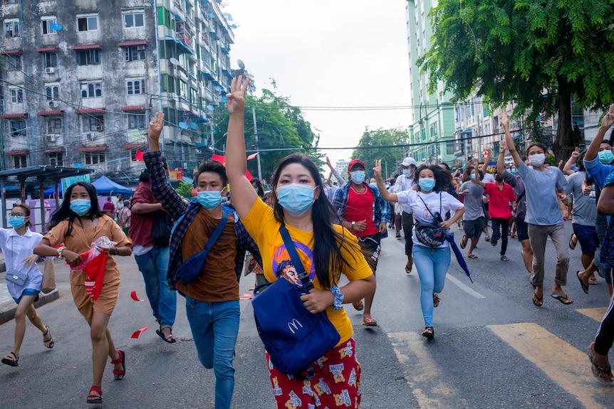 A group of young people in Myanmar wearing face masks hold their hands up in a three-finger salute