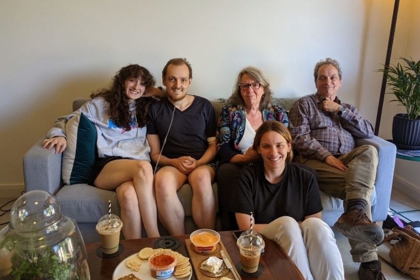 Young man with oxygen sitting on a couch surrounded by his mum, dad, sister and girlfriends 