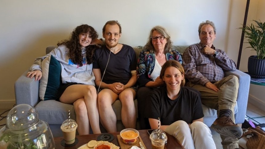 Young man with oxygen sitting on a couch surrounded by his mum, dad, sister and girlfriends 