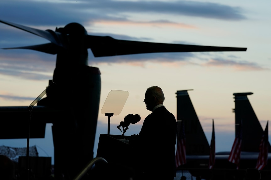 President Joe Biden speaks on a podium in front of the presidental plane.