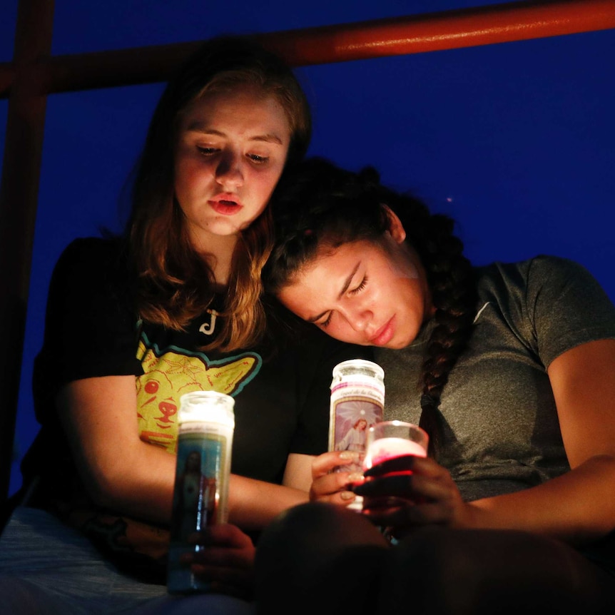 Two young girls lean against each other while holding candles.