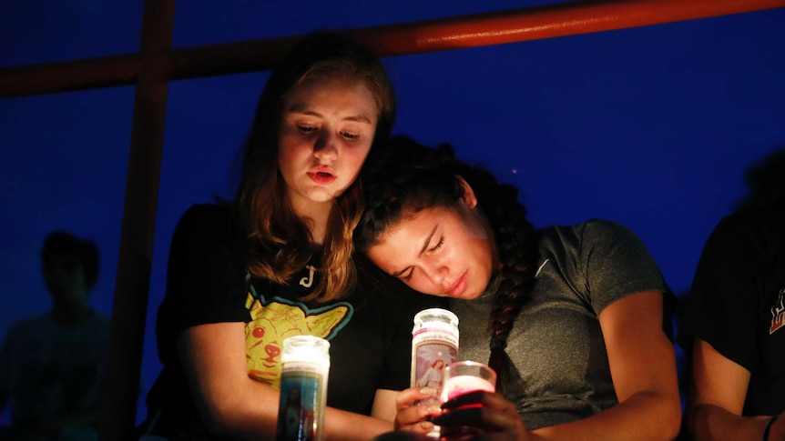 Two young girls lean against each other while holding candles.