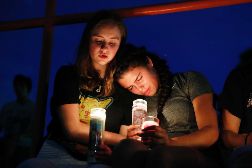 Two young girls lean against each other while holding candles.