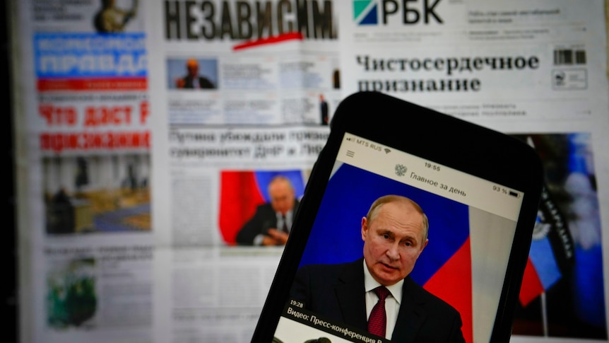 The app of the Russian government newspaper is displayed on an iPhone screen with newspapers in the background.