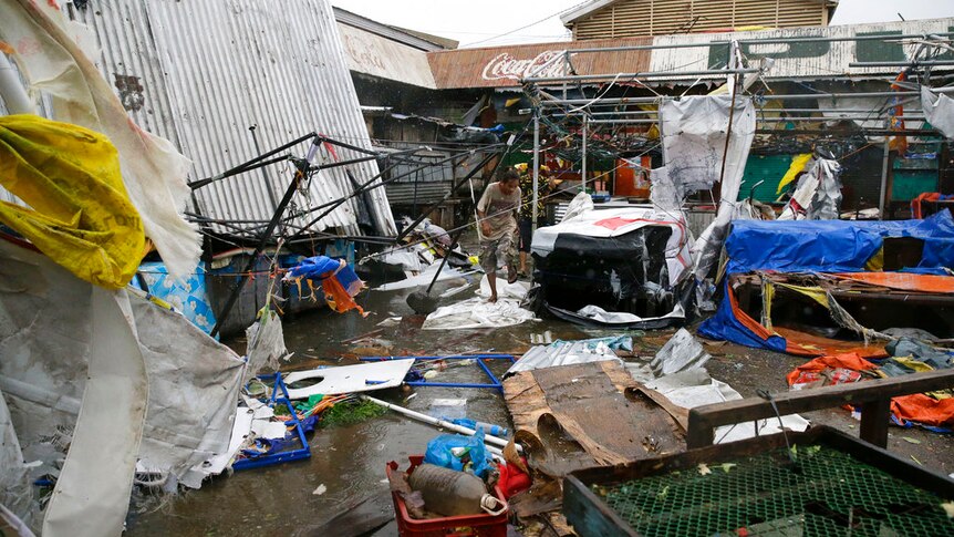 Residents walk along destroyed stalls at a public market due to strong winds.